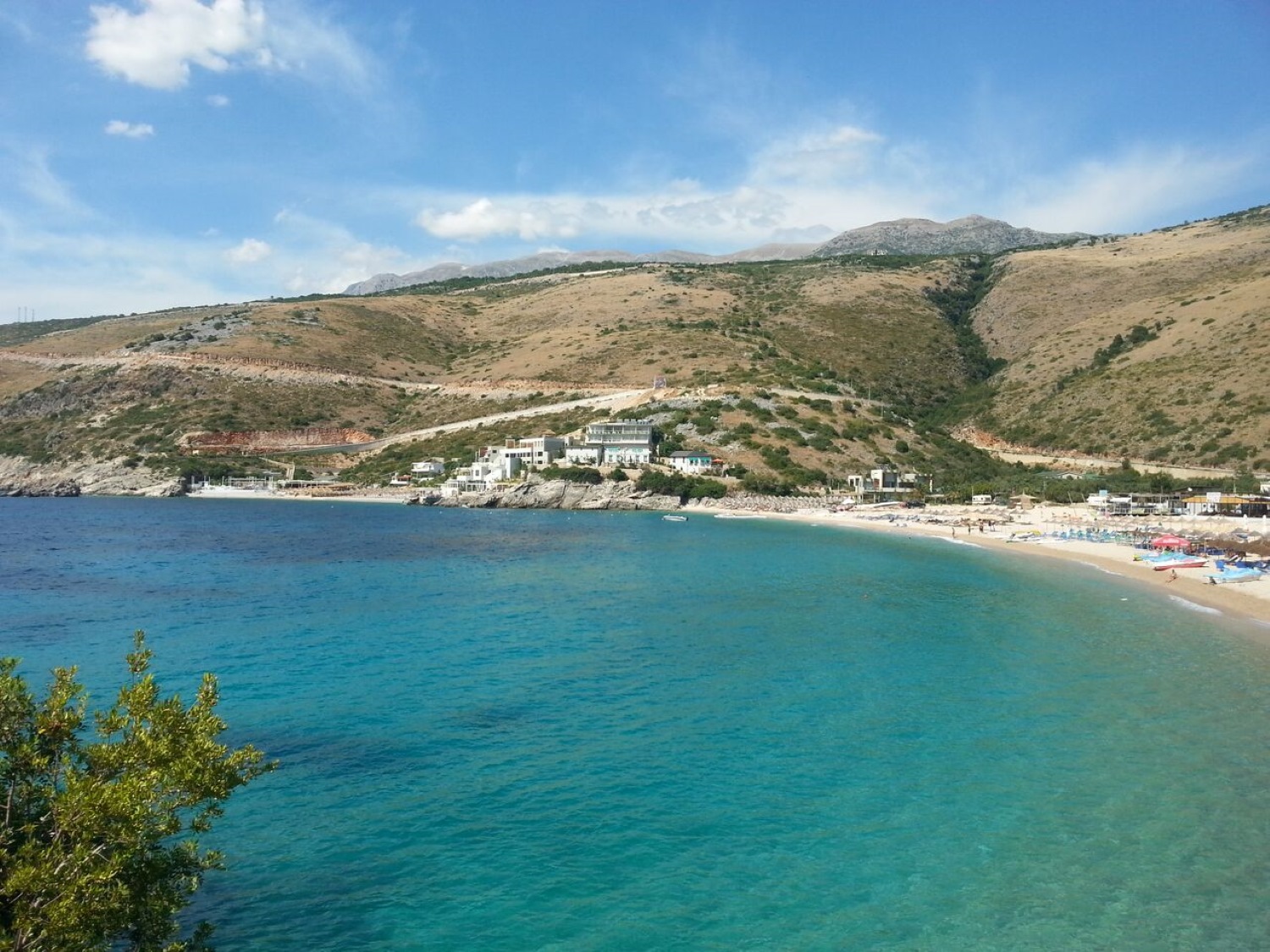 Jale Beach Albania — beach bars and swimmers in the clear turquoise cove backed by olive groves