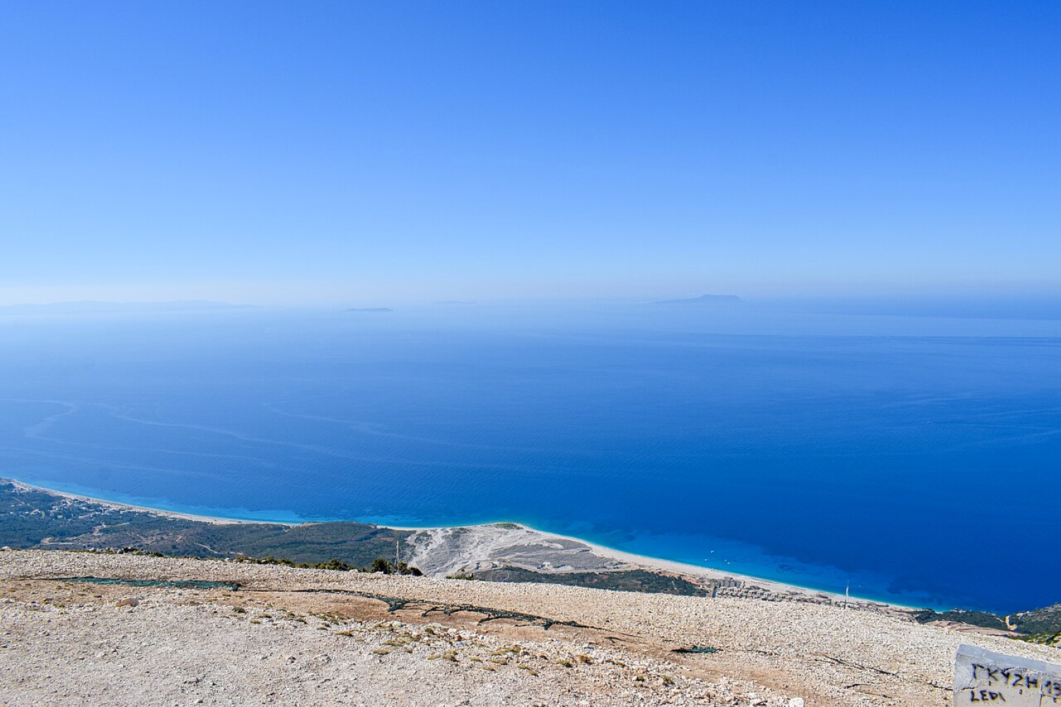 Palasë Beach Albania — pebble shore below limestone cliffs with Greek islands visible on the horizon